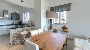 Une cuisine moderne avec un îlot central, des chaises blanches, une table à manger en bois et un luminaire suspendu.