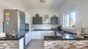 Une cuisine moderne dotée d’un îlot central, d’appareils électroménagers en acier inoxydable et offrant une vue sur l’extérieur grâce à une fenêtre.