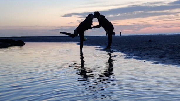 Silueta de dos personas formando un corazón con las manos en la playa al atardecer.