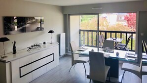 Un comedor moderno con una mesa y sillas de vidrio, un armario blanco con detalles negros, y vistas a un jardín a través de amplios ventanales.