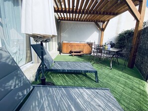 Eine überdachte Terrasse mit einer Holz-Pergola, einem Whirlpool und einem Essbereich mit Metallstühlen und einem Tisch.