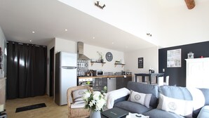 Ein modernes Wohnzimmer mit einem grauen Sofa, einem Couchtisch mit Blumen und einer Küche im Hintergrund.
