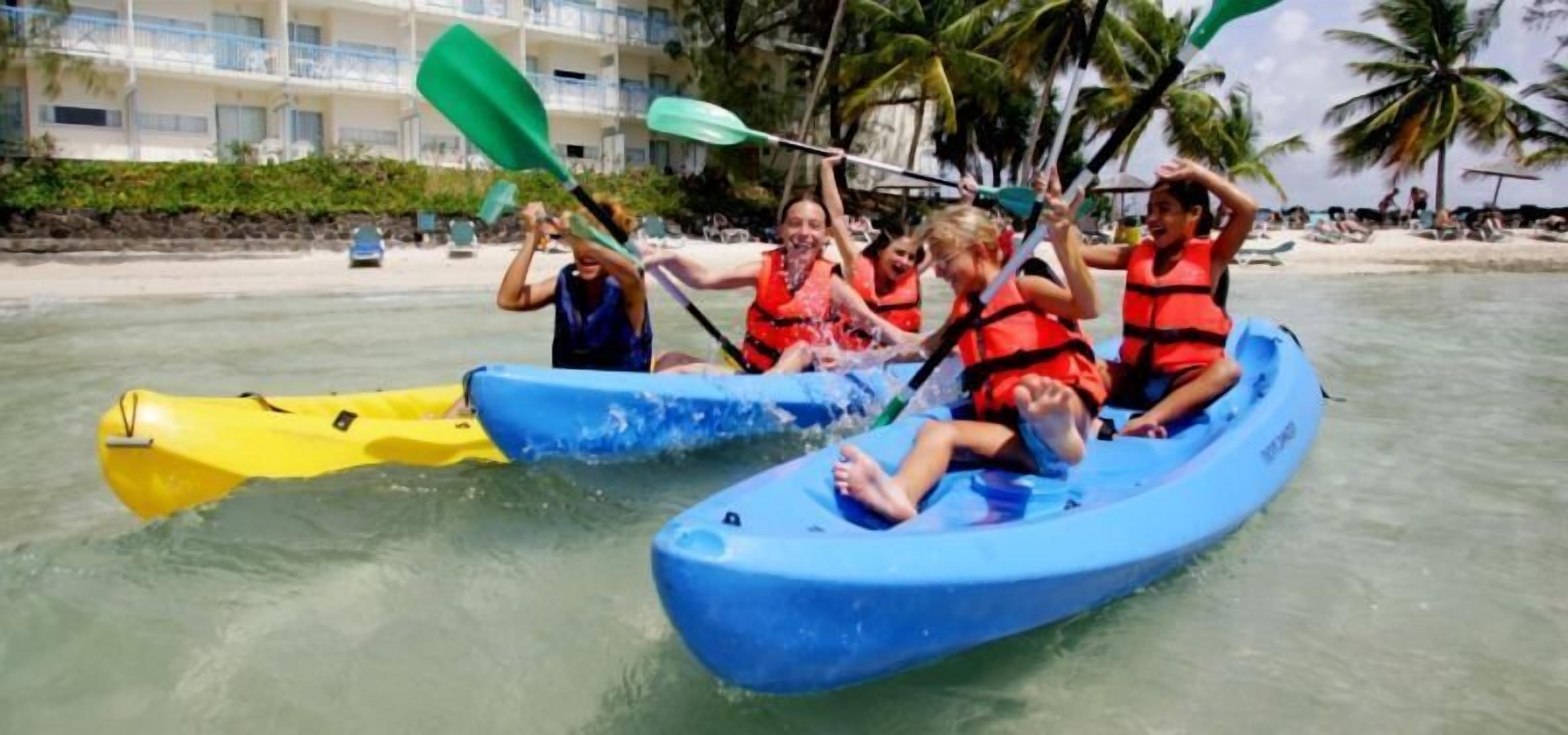 Eine Gruppe Menschen paddelt mit dem Kajak auf ruhigem Wasser, dabei tragen sie Rettungswesten und steuern ein blau-gelbes Kajak.