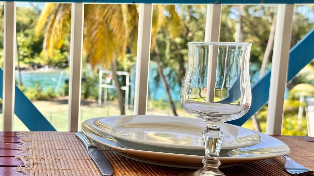 Une table dressée avec un verre, une assiette et des couverts, donnant sur une piscine et une végétation luxuriante.