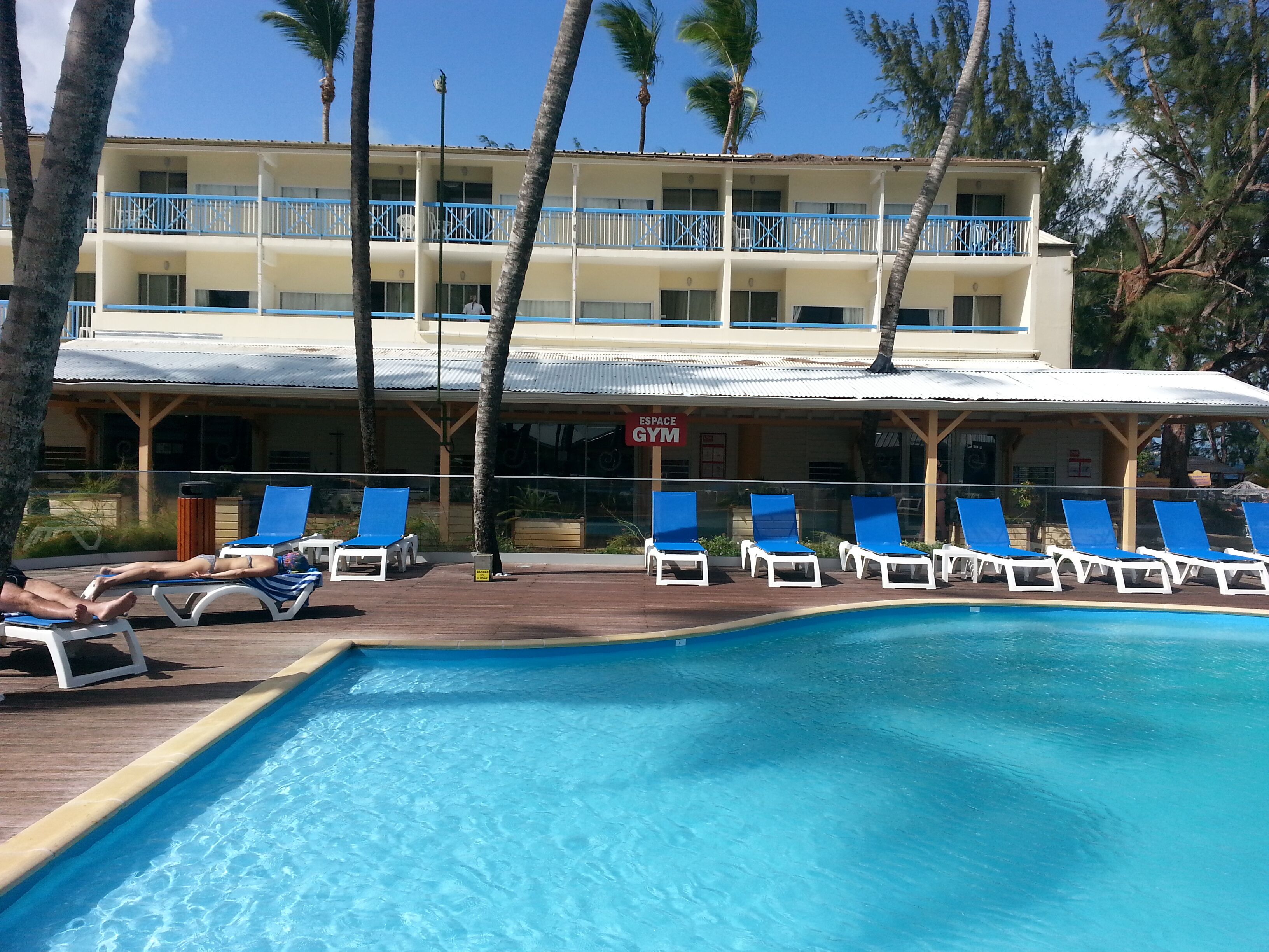 A pool area with lounge chairs and a building with a gym sign.