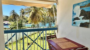 Un balcon donnant sur une piscine et des palmiers, un tableau représentant une vague et une table avec un tapis.