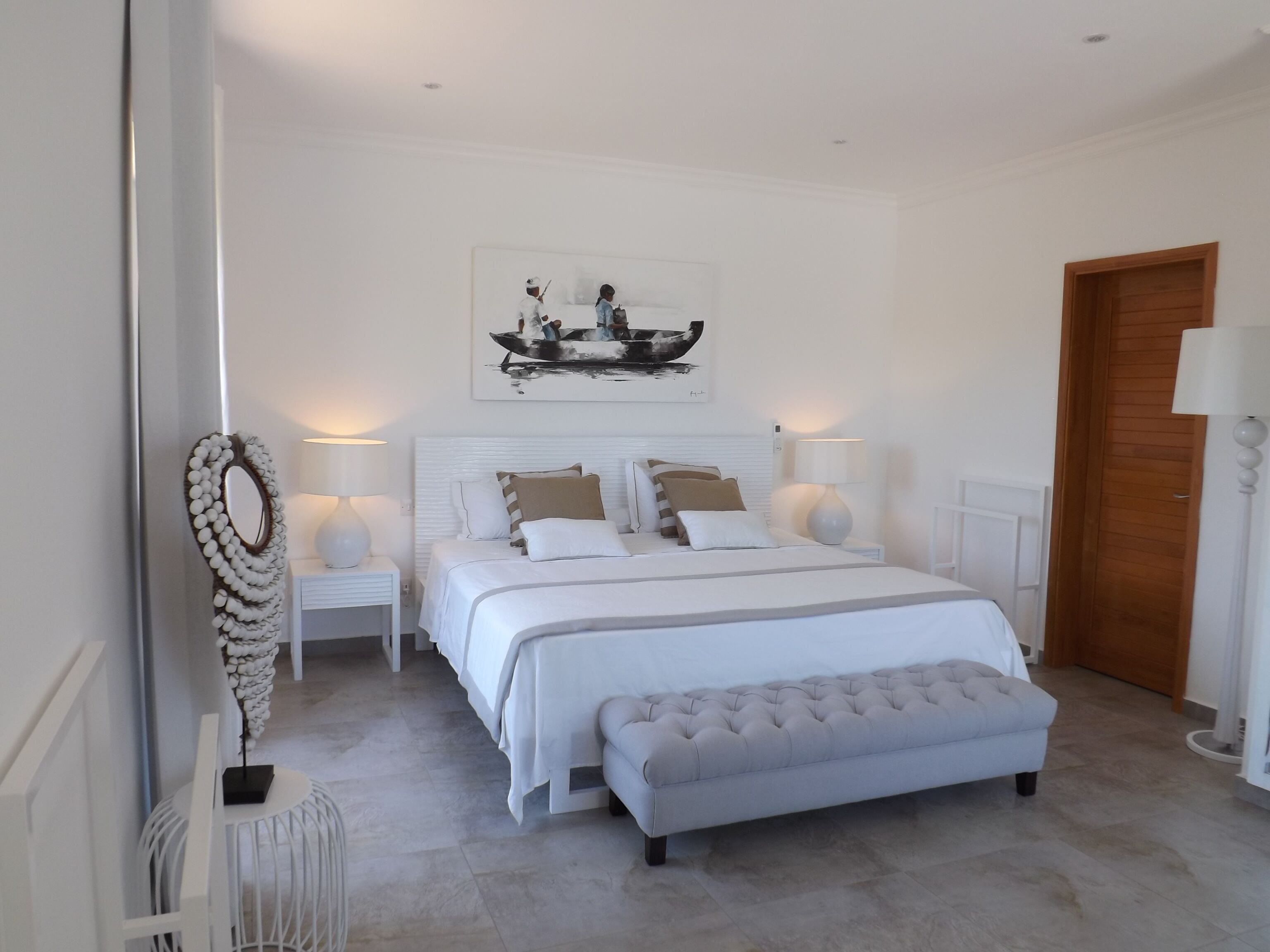 A bedroom with a large bed, bedside tables, a bench, and a painting on the wall.