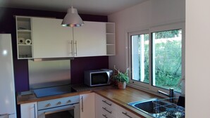 A compact kitchen with a microwave, a small stove, a sink, and a window providing a view of greenery outside. - Small independent house in the countryside, near Saint Emilion, sleeps 4 (Lagorce)
