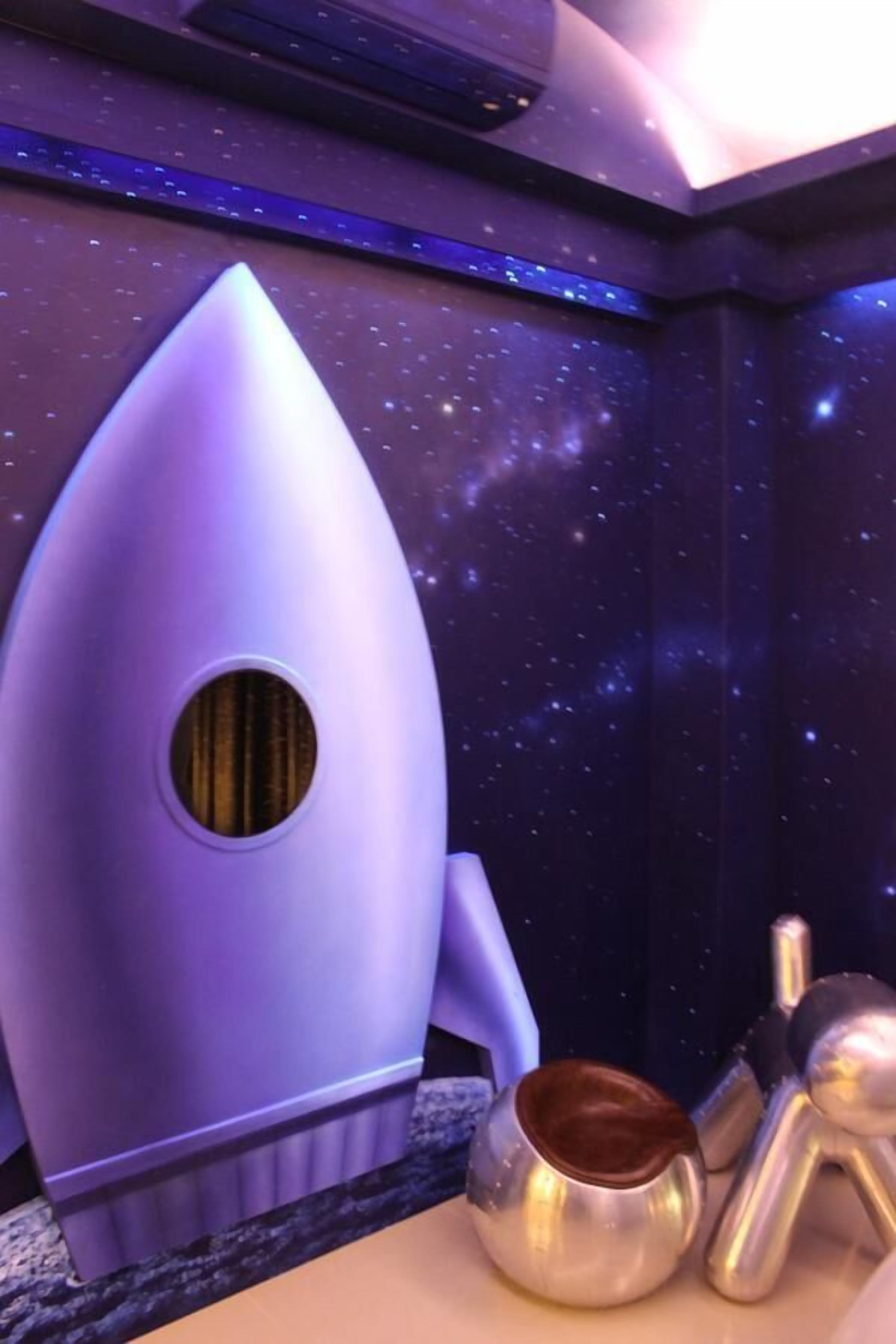 A room with a space-themed design, including a rocket-shaped object and a small metallic sculpture.
