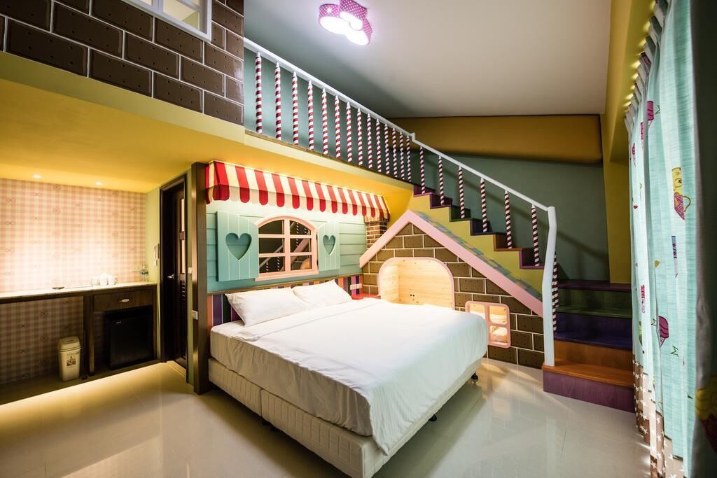 A bedroom with a bed, a small desk, a staircase, and a window with curtains.