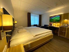 Una habitación de hotel con cama, escritorio, televisor y ventana con cortinas.