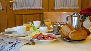 A breakfast setup with a newspaper, a plate of ham, a croissant, a coffee pot, a glass of orange juice, and a vase with flowers. - Wieting (Oldenburg)