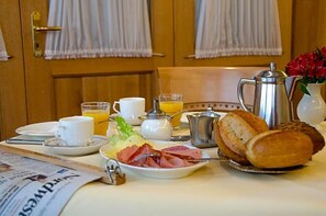 A breakfast setup with a newspaper, a plate of ham, a croissant, a coffee pot, a glass of orange juice, and a vase with flowers. - Wieting (Oldenburg)