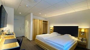 A hotel room with a bed, bedside table, desk, chair, and wardrobe. - Wieting (Oldenburg)