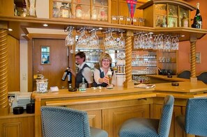 Zona de bar con mobiliario de madera, una barra y copas colgando.