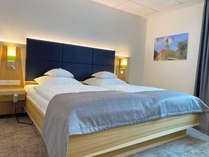 A hotel room with a bed, bedside lamps, a nightstand, and a painting on the wall. - Wieting (Oldenburg)