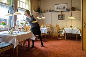 A restaurant with tables set for dining, a waiter attending to guests, and a view of the city through large windows. - Wieting (Oldenburg)