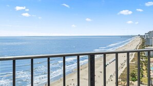 A coastal view from a balcony overlooking a beach with a pier, clear skies, and a few buildings in the distance. - Palace 1503 (Myrtle Beach)