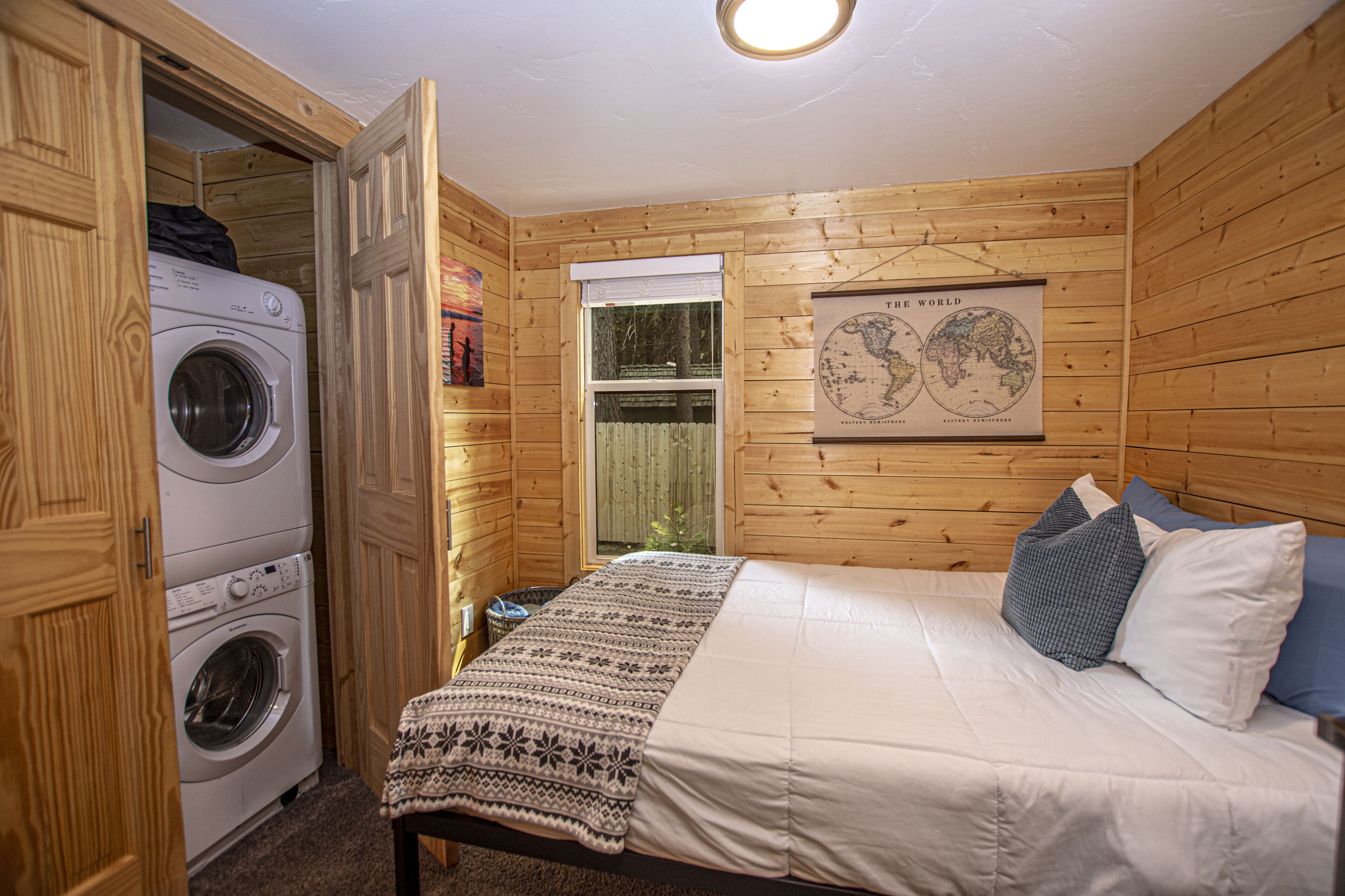 A compact room with a bed, a washing machine, and a window.