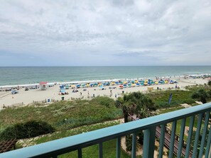 A beach with umbrellas and lounge chairs, a fence, and a view of the ocean.