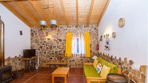 A rustic interior with a stone wall, wooden furniture, a television, and a fireplace. - Digne Yellow Villa, Pool, BBQ (Aljezur)