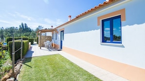A modern house with a white exterior, a tiled roof, and a small patio area with a table and chairs. - Digne Yellow Villa, Pool, BBQ (Aljezur)