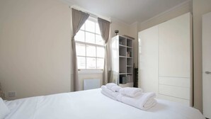 Ett hotellrum med en snyggt bäddad säng, ett fönster med gardiner, en inbyggd bokhylla och en garderob.