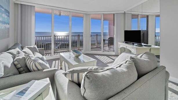 Une chambre d’hôtel moderne dotée d’un balcon, d’une télévision à écran plat et d’un coin salon offrant une vue sur l’océan.
