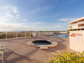 Un área de spa con un jacuzzi, una piscina y una cerca blanca.