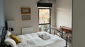 A bedroom with a bed, a desk, a chair, and a window with a view of buildings.