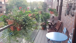 A balcony with potted plants, a wooden bench, and a small table.