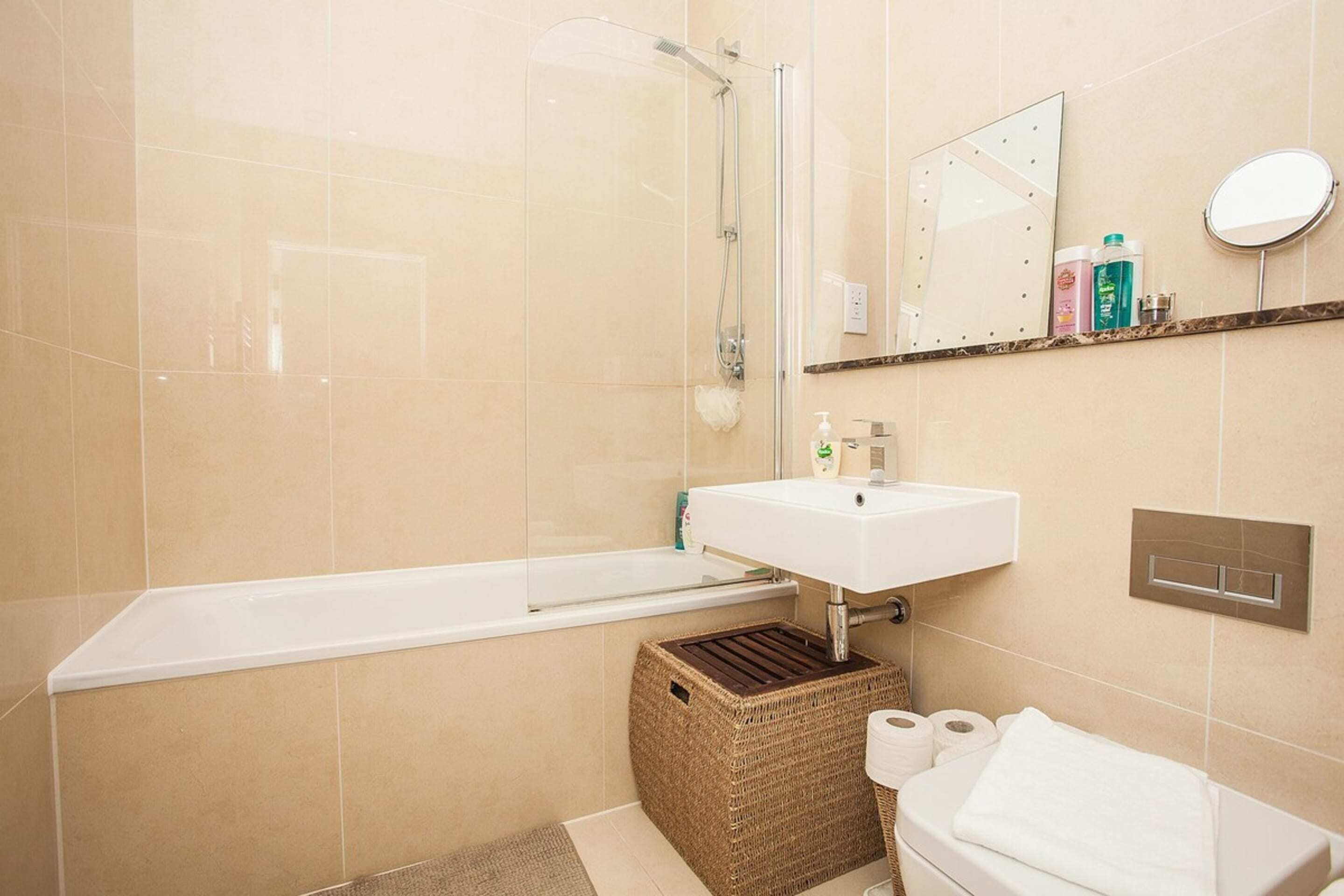 Ein Badezimmer mit Badewanne, einer Duschkabine, einem Waschbecken, einem Spiegel und Pflegeprodukten auf einem Regal.