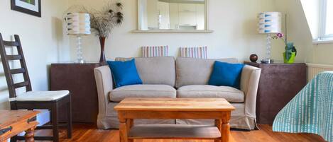 A cozy living room with a wooden coffee table, a sofa with blue cushions, a chair, and a lamp.