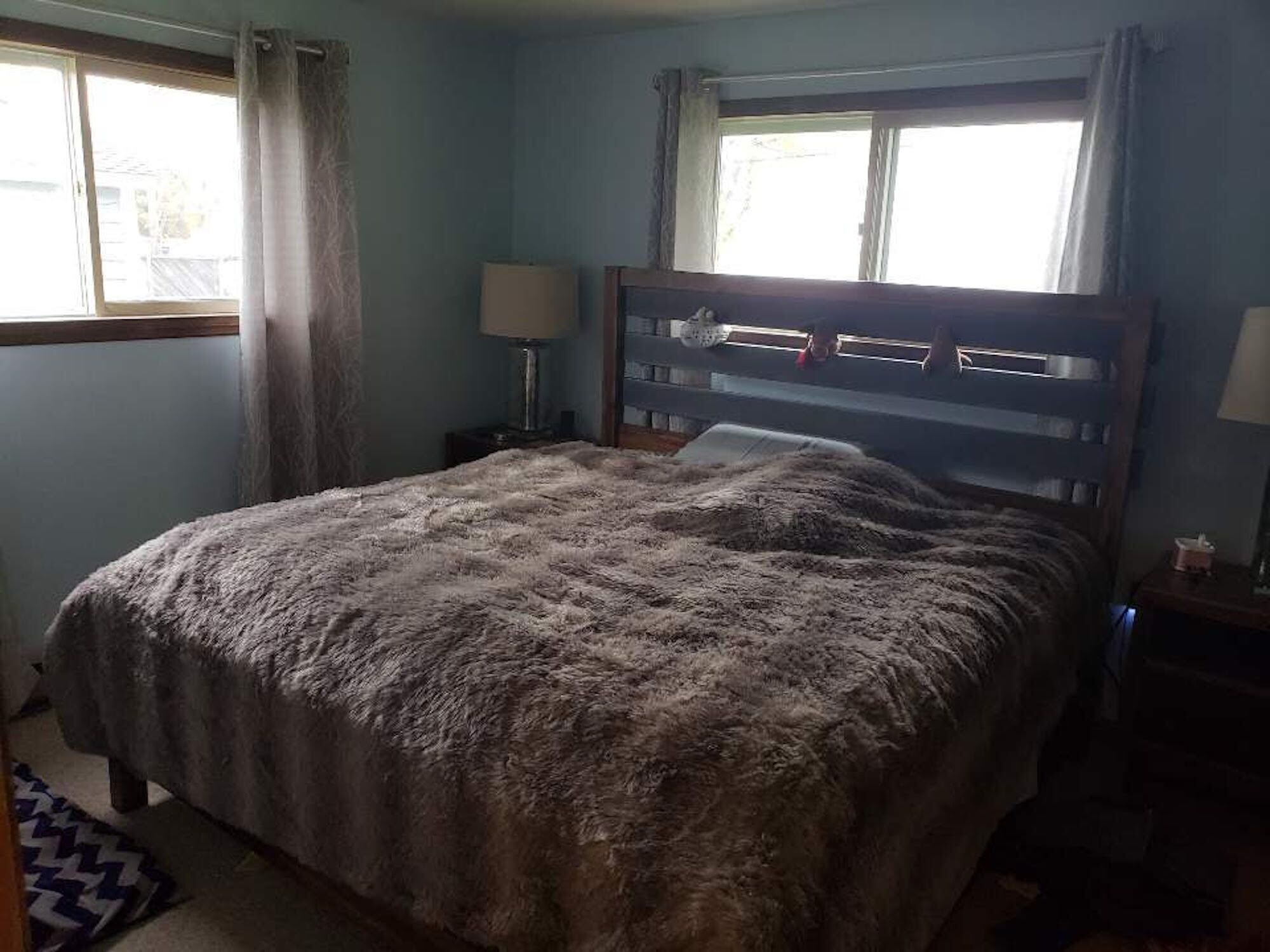 A bedroom with a large bed, two bedside tables, a window with curtains, and a nightstand with a lamp.