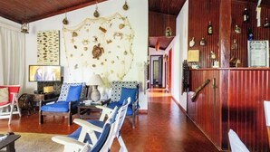 Un vaste espace de vie doté d’un plafond en bois, d’un grand mur décoré de coquillages et d’étoiles de mer, et d’un coin bar avec des bouteilles et un menu.
