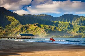 A beach with a wooden pier and a building, surrounded by mountains.