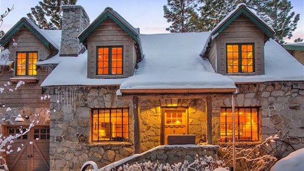 Una casa de piedra con tejado cubierto de nieve y ventanas iluminadas desde el interior.