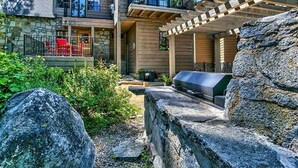 Una casa de dos pisos con fachada de piedra, un patio con sillas rojas y una parrilla.