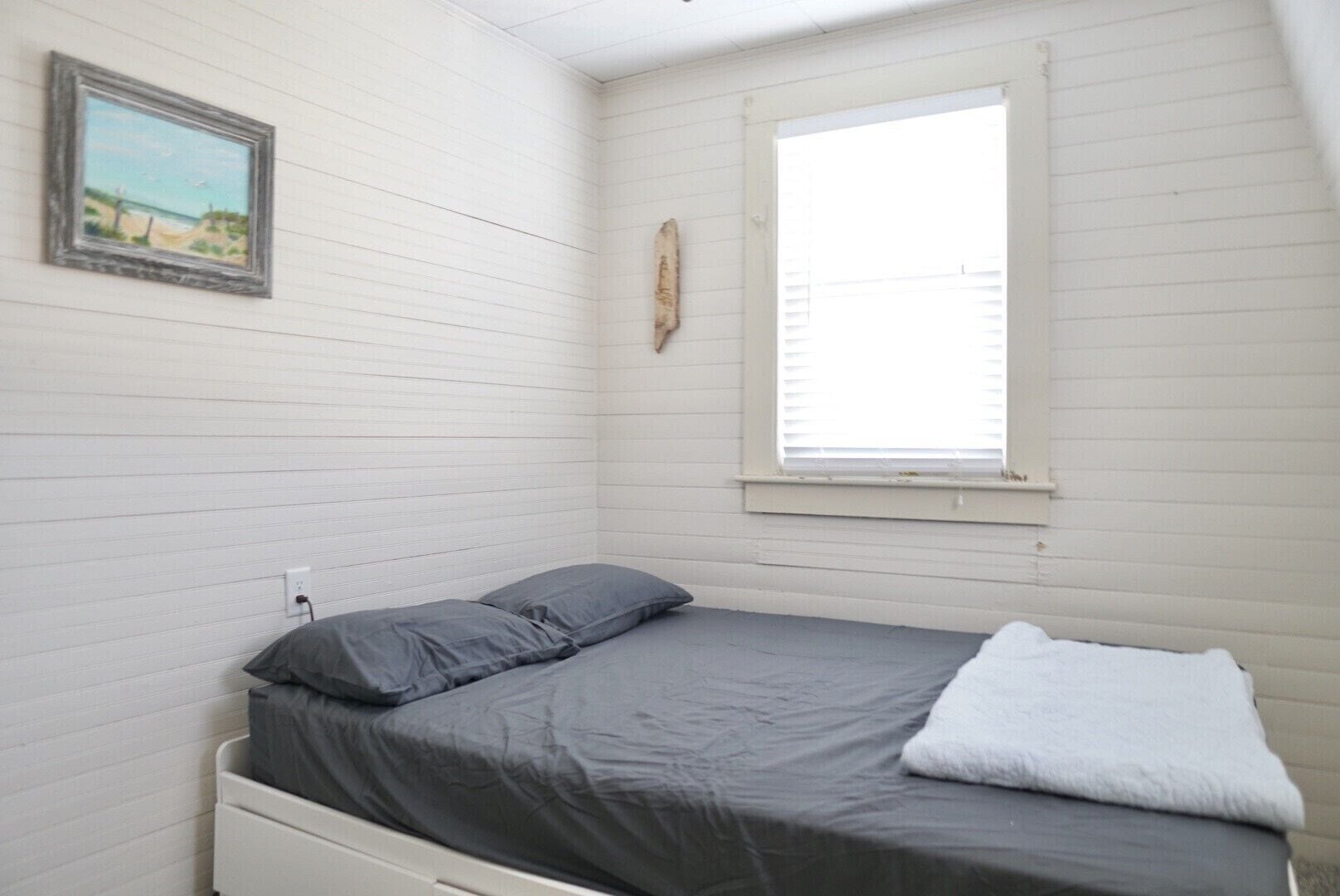 Una habitación pequeña con cama individual, paredes blancas y una ventana.
