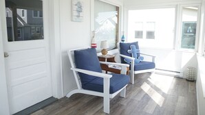 Quarto com porta branca, duas poltronas estofadas em azul, uma mesa pequena com abajur e uma janela com persianas.