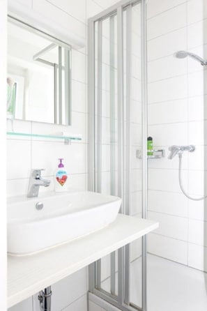 A modern bathroom with a white sink, a glass shower enclosure, and a mirror above the sink. - Hotel-Restaurant Wiendl (Regensburg)
