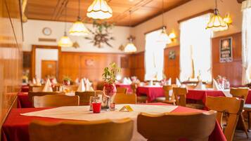 Ein Restaurant mit mehreren Tischen, jeder Tisch ist mit einer roten Tischdecke, weißen Servietten und einer Speisekarte bedeckt.