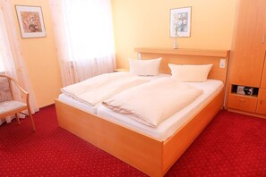 A double bed with white linens, a wooden headboard, a red carpeted floor, a wooden wardrobe, and two framed pictures on the wall. - Hotel-Restaurant Wiendl (Regensburg)