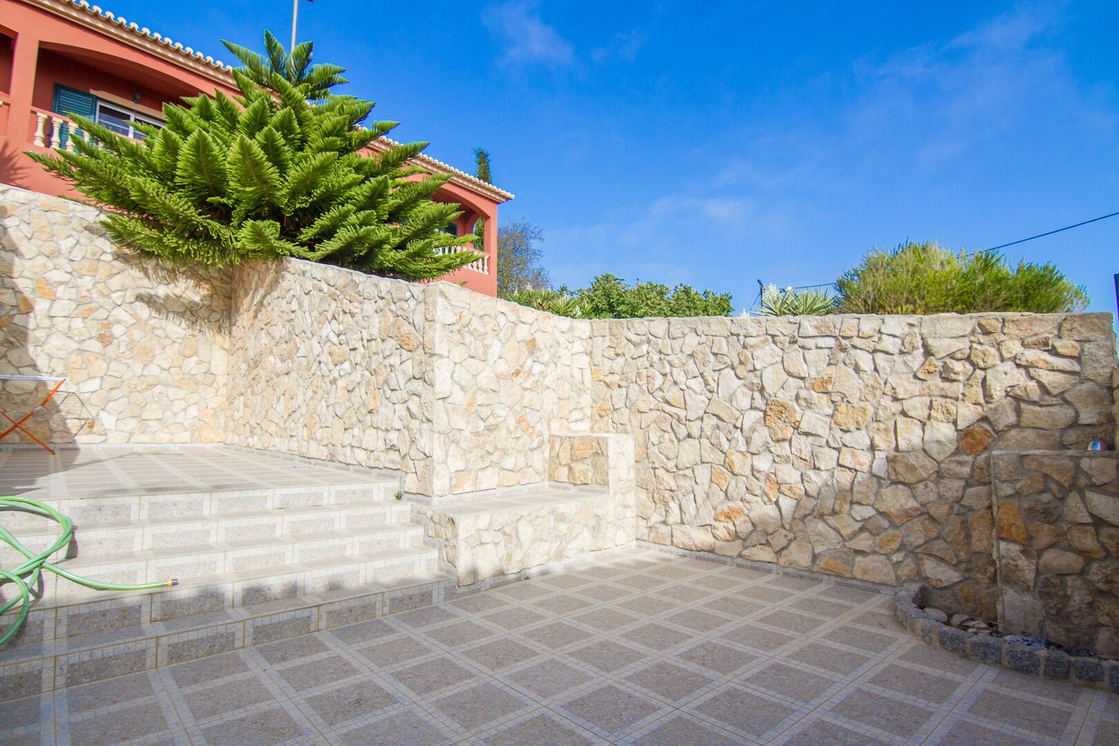 A stone wall with steps leading to a house with a red facade.