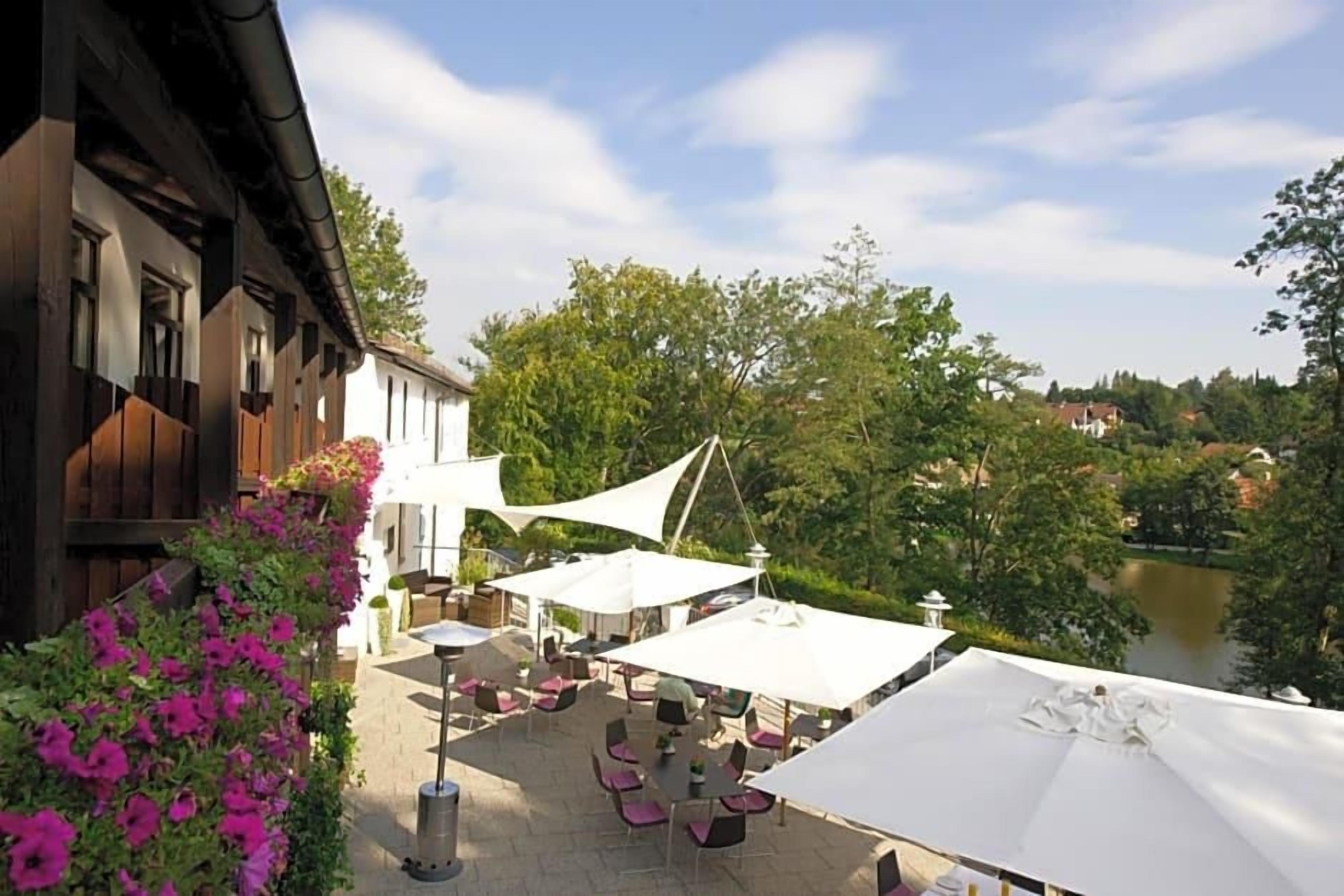 Un espace extérieur aménagé avec des tables et des parasols, offrant une vue sur une rivière et la verdure environnante.