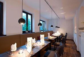 Un restaurante con mesas largas comunitarias, iluminación colgante y grandes ventanales.