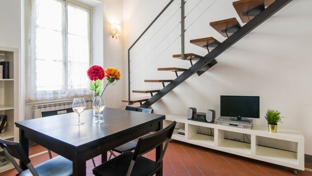 Una sala moderna con escalera, una mesa de comedor con sillas, un televisor y una estantería.