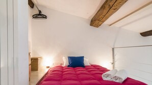 Un dormitorio pequeño y acogedor con una colcha roja, una almohada azul y un par de toallas enrolladas sobre la cama.