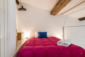 A small, cozy bedroom with a red bedspread, a blue pillow, and a pair of rolled towels on the bed. - Comfortable and bright 80 sqm apartment, able to comfortably accommodate up to 5 people, is located on the third and top floor of a late 19th century building with lift. The property is located in an elegant neighborhood near the historic center of Flore (Firenze)