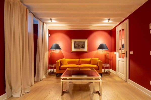 Une pièce avec un mur rouge, un plancher en bois, un canapé, deux lampes et un tableau encadré accroché au mur.